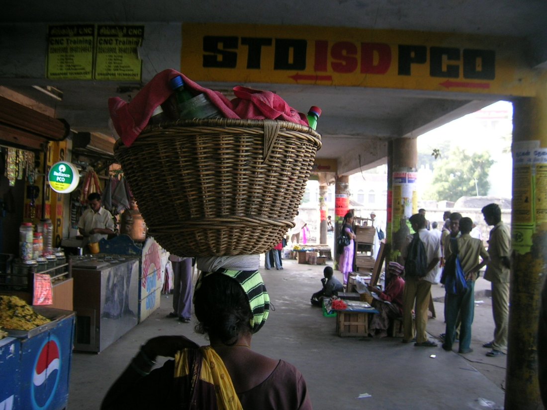 woman carrying her wares on her head in a bus station in the south of India. She starts the day knowing that the competition is fierce...